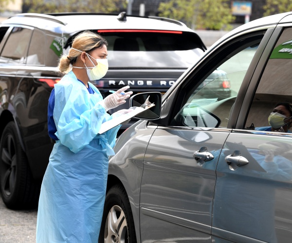 LOS ANGELES, CA - APRIL 13:  A worker wearing personal protective equipment gathers the tests administered from a car as Mend Urgent Care hosts a drive-thru testing for the COVID-19 virus at the Westfield Fashion Square on April 13, 2020 in the Sherman Oaks neighborhood of Los Angeles, California. Los Angeles County 'safer at home' orders remain in effect through May 15 to stop the spread of coronavirus during the worldwide pandemic.  (Photo by Kevin Winter/Getty Images)