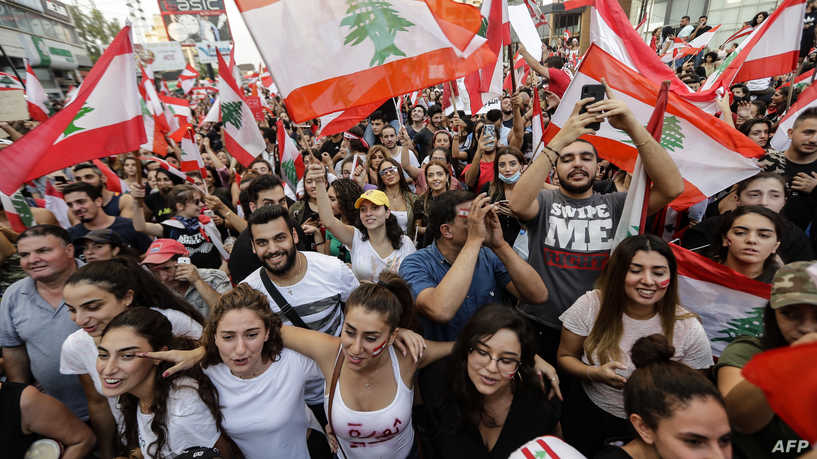 Lebanese demonstrators wave national flags on a highway linking Beirut to north Lebanon, in Zouk Mosbeh on October 19, 2019, a day after demonstrations swept through the eastern Mediterranean country in protest against dire economic conditions. - Thousands of protesters outraged by corruption and proposed tax hikes burned tyres and blocked major highways in Lebanon on Friday, prompting the premier to give his government partners three days to support a reform drive. (Photo by JOSEPH EID / AFP)