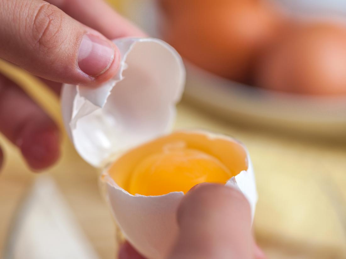 a-hand-holding-a-cracked-egg-showing-a-yolk