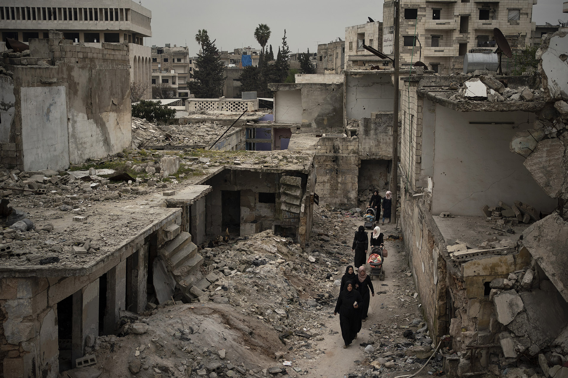In this Thursday, March 12, 2020 photo, women walk in a neighborhood heavily damaged by airstrikes in Idlib, Syria. Idlib city is the last urban area still under opposition control in Syria, located in a shrinking rebel enclave in the northwestern province of the same name. Syria’s civil war, which entered its 10th year Monday, March 15, 2020, has shrunk in geographical scope -- focusing on this corner of the country -- but the misery wreaked by the conflict has not diminished. (AP Photo/Felipe Dana)