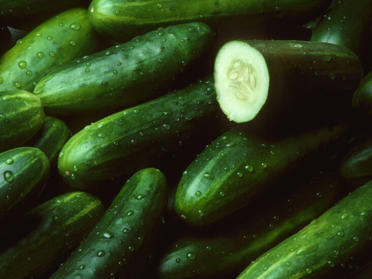 A pile of fresh cucumbers lying diagonally with drops of water with one cut open