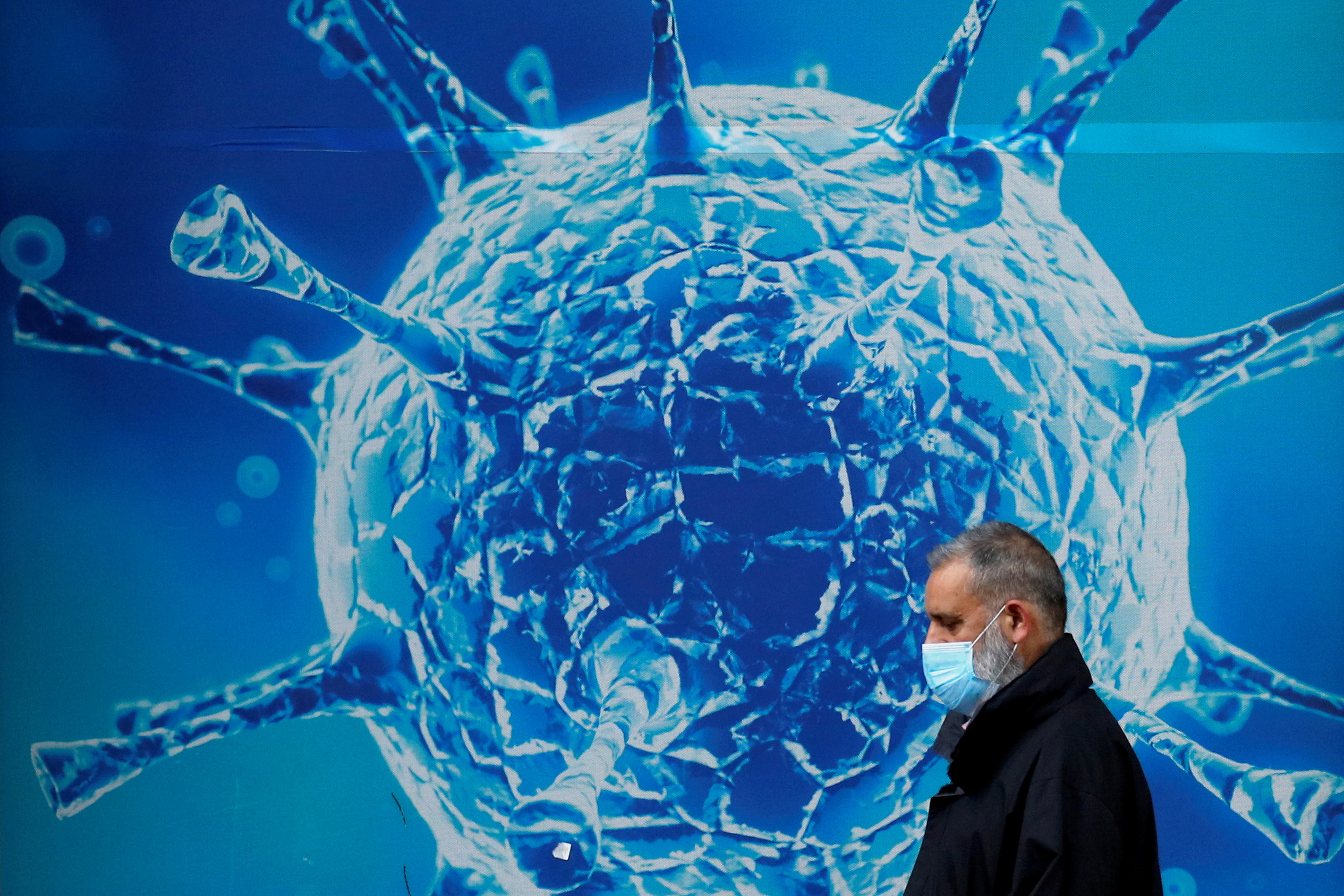 FILE PHOTO: A man wearing a protective face mask walks past an illustration of a virus outside a regional science centre amid the coronavirus disease (COVID-19) outbreak, in Oldham, Britain August 3, 2020. REUTERS/Phil Noble