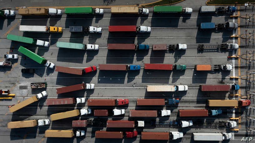 (FILES) In this file aerial image taken on October 14, 2021 trucks transport cargo containers at the Port of Baltimore in Baltimore, Maryland. - With US prices rising at a rate not seen in decades, President Joe Biden's administration is looking for ways to turn the tide. (Photo by Brendan Smialowski / AFP)