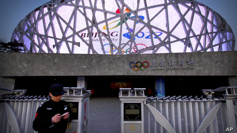 A security guard checks his cellphone in front of the Beijing National Stadium, also known as the Birds Nest, as a promotional video for the proposed Beijing 2022 Winter Olympics plays on the side of the stadium in Beijing, Saturday, March 28, 2015. The International Olympic Committee (IOC) concluded a 5-day visit on Saturday to inspect Beijing's bid for the 2022 Winter Olympics. (AP Photo/Mark Schiefelbein)