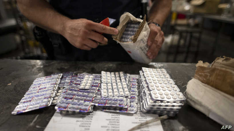 An officer from the US Customs and Border Protection, Trade and Cargo Division finds Oxycodon pills in a parcel at John F. Kennedy Airport's US Postal Service facility on June 24, 2019 in New York. - In a windowless hangar at New York's JFK airport, dozens of law enforcement officers sift through packages, looking for fentanyl -- a drug that is killing Americans every day. The US Postal Service facility has become one of multiple fronts in the United States' war on opioid addiction, which kills tens of thousands of people every year and ravages communities. (Photo by Johannes EISELE / AFP)