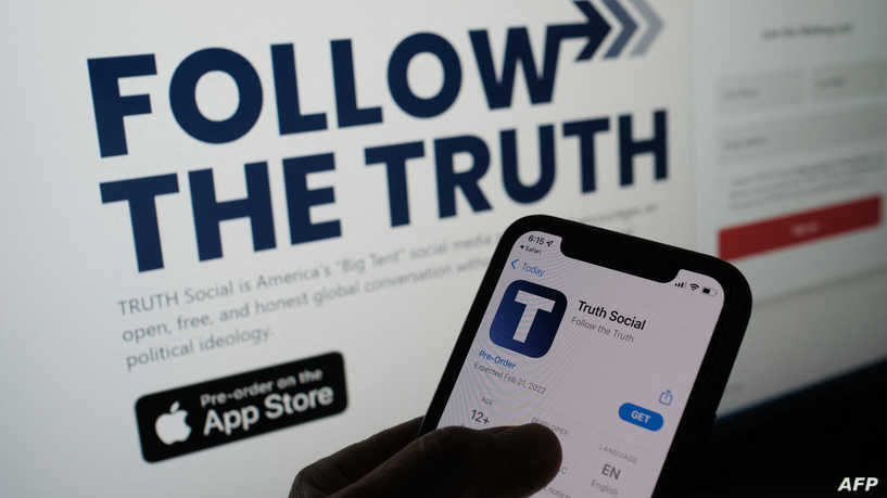 This illustration photo shows a person checking the app store on a smartphone for "Truth Social", with it's website on a computer screen in the background, in Los Angeles, October 20, 2021. - Former US president Donald Trump announced plans on October 20 to launch his own social networking platform called "TRUTH Social," which is expected to begin its beta launch for "invited guests" next month. The long-awaited platform will be owned by Trump Media & Technology Group (TMTG), which also intends to launch a subscription video on-demand service that will feature "non-woke" entertainment programming, the group said in a statement. (Photo by Chris DELMAS / AFP)