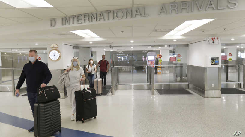 Passengers wearing surgical masks exit from the International Arrivals door, Friday, March 13, 2020, at Miami International Airport in Miami. (AP Photo/Wilfredo Lee)