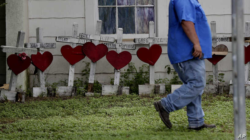 A man passes old memorial crosses on the side of a church building following a dedication ceremony for a new sanctuary and memorial room at the First Baptist Church in Sutherland Springs, Texas, Sunday, May 19, 2019. In 2017 a gunman opened fire at the church and killed more than two dozen congregants. (AP Photo/Eric Gay)