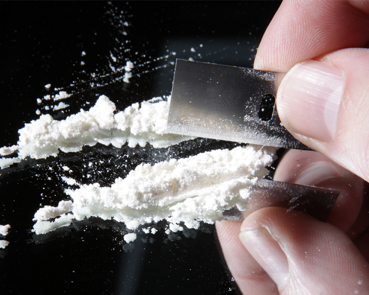 cocaine or other drugs cut with razor blade on mirror. hand dividing white powder narcotic