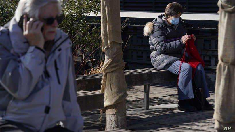 A woman wears a mask while knitting in a park in New York, Wednesday, Feb. 9, 2022. New York Gov. Kathy Hochul announced Wednesday that the state will end a COVID-19 mask mandate requiring face coverings in most indoor public settings, but will keep masking rules in place in schools for now. (AP Photo/Seth Wenig)